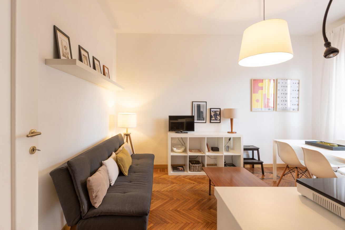 Una sala de estar moderna con un sofá, una televisión, un comedor y una pared blanca con estanterías.