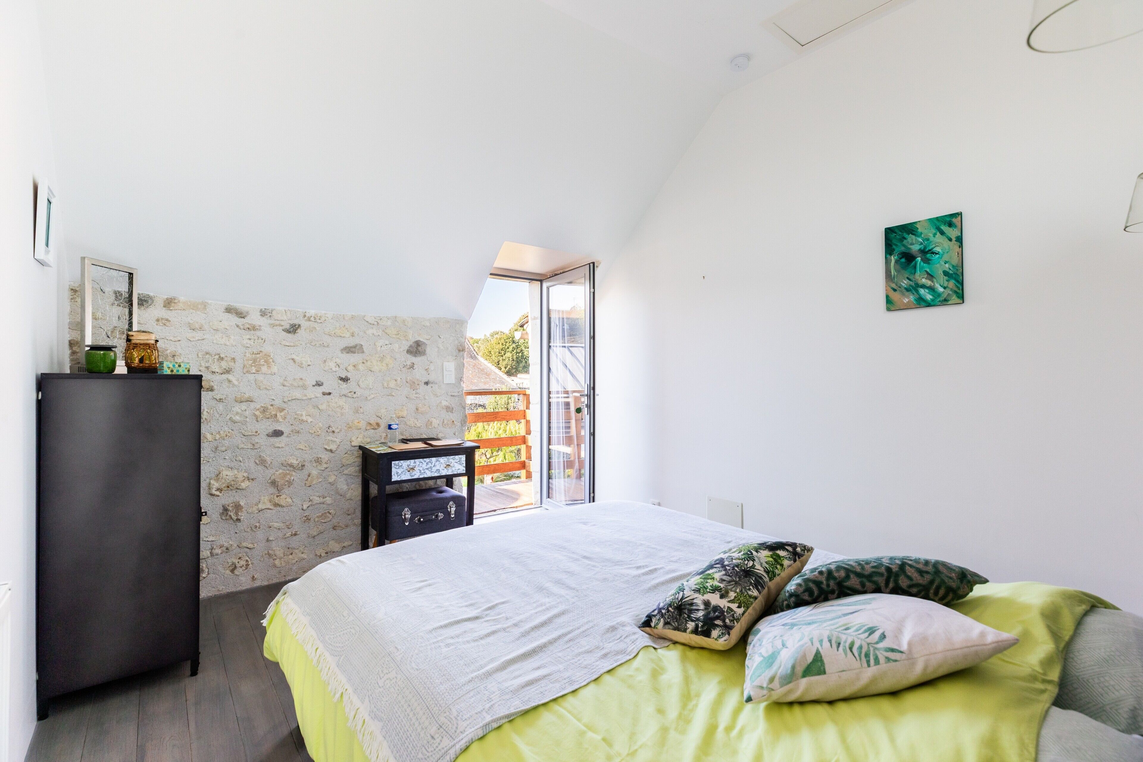 Un dormitorio con cama, cómoda, pared de piedra y puerta que da a un balcón.