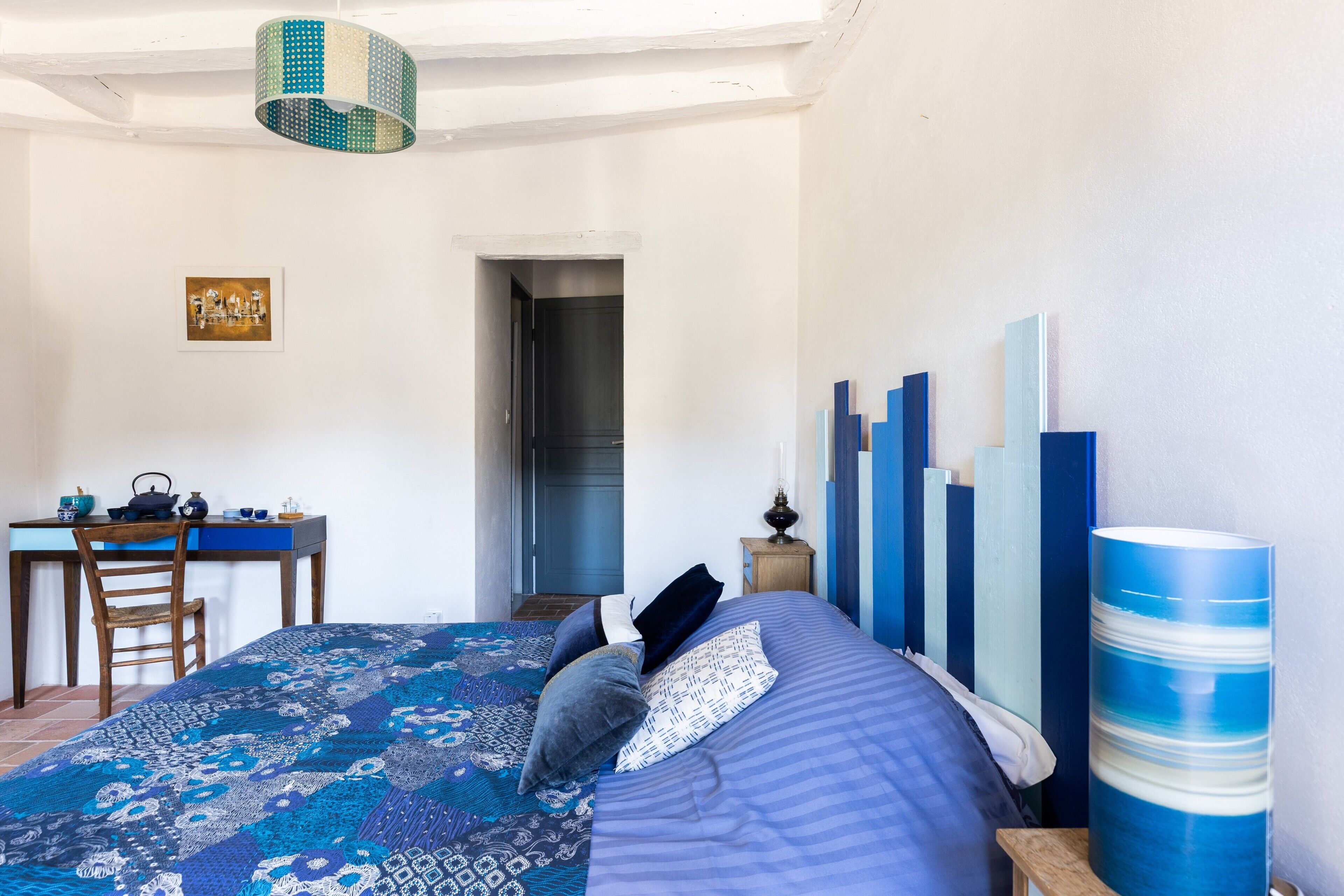 Une chambre avec un lit, un bureau et une chaise. Une porte donne accès à une autre pièce.