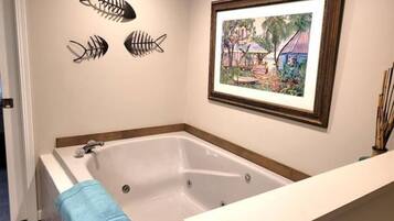 A bathroom with a large bathtub, a framed painting on the wall, and decorative fish skeletons.