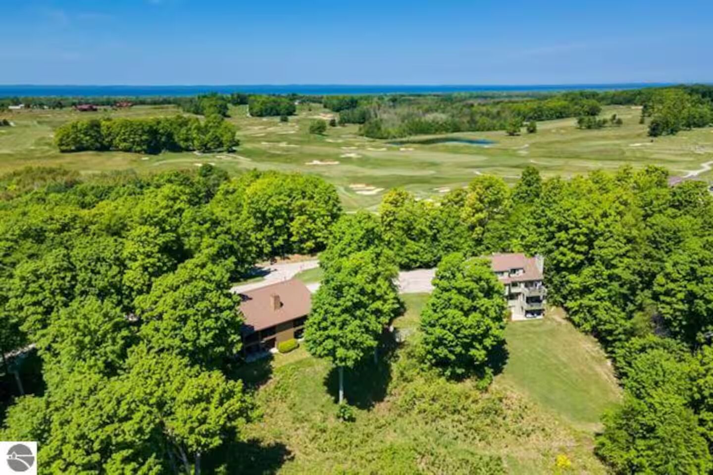 Vista aérea de um campo de golfe com duas construções rodeadas por árvores densas.