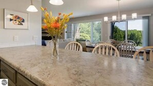A modern kitchen with a marble countertop, a vase of flowers, and a dining area with chairs. - 2BR Escape Torch Lake Views Golf 755 (Kewadin)