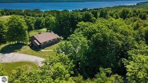 A house surrounded by dense trees with a clear view of a large body of water in the background. - 2BR Escape Torch Lake Views Golf 755 (Kewadin)