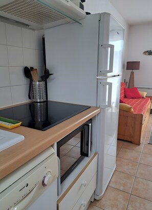 A compact kitchen with a built-in stove, a refrigerator, and a dining area with a bed. - Holiday Home 'Duplex Near Lake La Raviège' with Private Terrace and Private Garden (La Salvetat sur Agout)