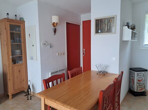 A dining area with a wooden table, red chairs, a cabinet with glass doors, a wall-mounted light, and a framed picture of kitchen utensils. - Holiday Home 'Duplex Near Lake La Raviège' with Private Terrace and Private Garden (La Salvetat sur Agout)