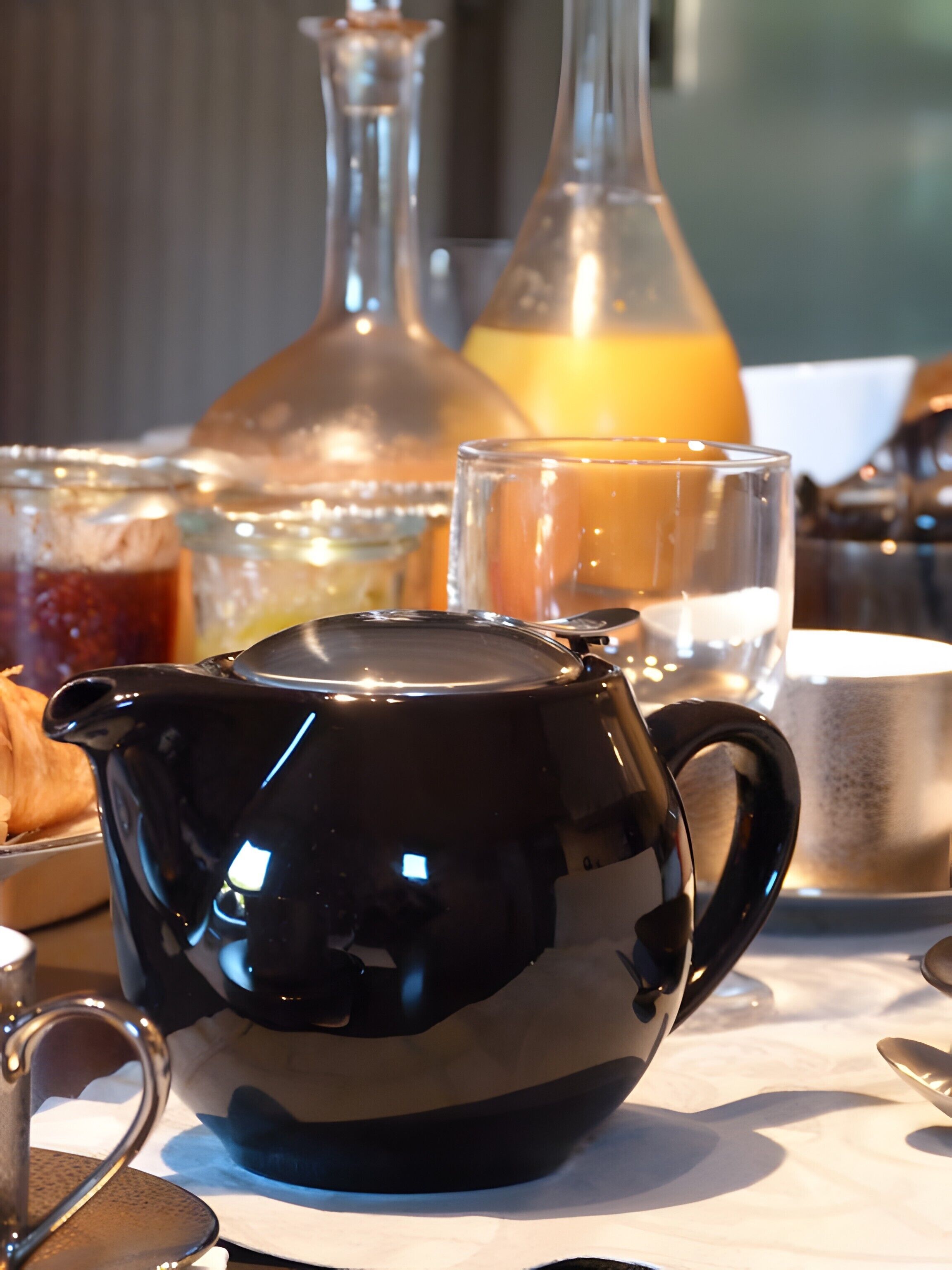 A black teapot on a table with a glass of orange juice and a glass of water.