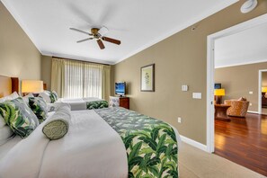 A hotel room with a bed, a ceiling fan, a television, and a view of the hallway.