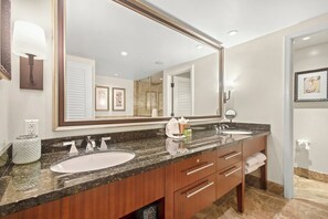 A bathroom with a large mirror, two sinks, a vanity with drawers, and a towel rack.