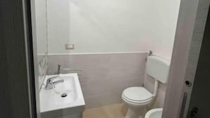 Ein kleines, kompaktes Badezimmer mit einem weißen Waschbecken, einer Toilette und einem Spiegel.