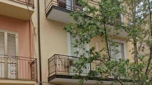 Ein mehrstöckiges Gebäude mit Balkonen und einem Baum im Vordergrund.