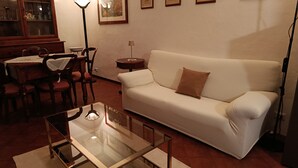 Un salon avec une table basse en verre, un canapé blanc, une table à manger avec des chaises et des tableaux encadrés accrochés au mur.
