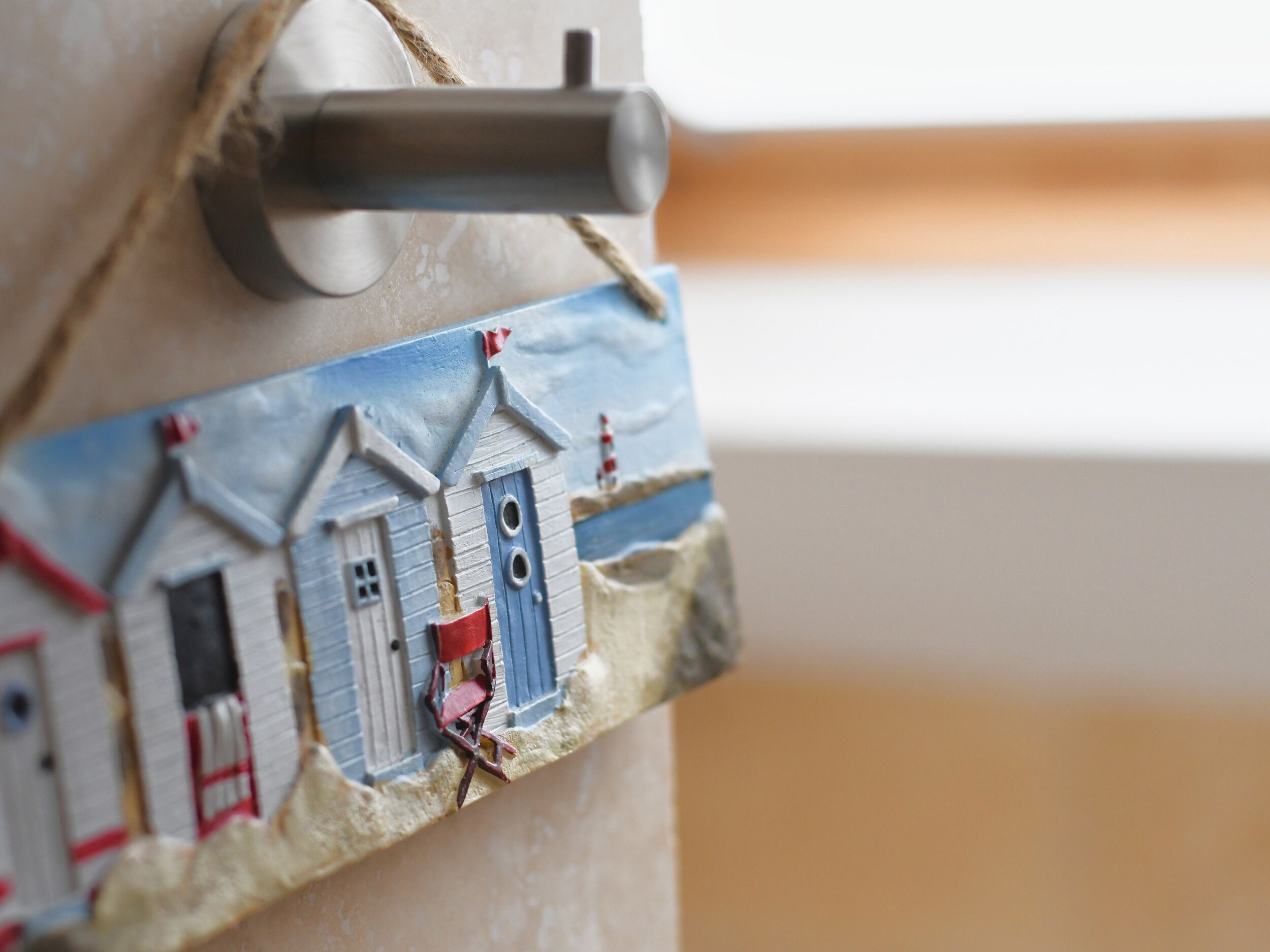 A close-up of a miniature seaside village model with a lighthouse, a red chair, and a small house with a blue door.