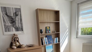 Een slaapkamer met een houten dressoir, een boekenkast, een rieten mand en een bed met beddengoed met een patroon.