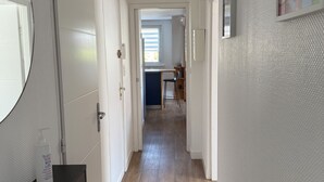 Een gang met een houten vloer, witte muren en een deur die leidt naar een kamer met een raam.