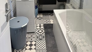 Een moderne badkamer met een witte wastafel, zwart-wit betegelde vloer, een wit toilet en een bad.
