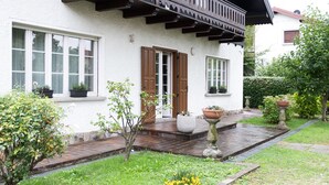 A white building with a wooden porch, potted plants, and a paved pathway. - Spacious vacation home in Tarcento - perfect for cyclists & hikers (Tarcento)