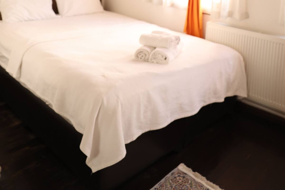 A bedroom with a wooden headboard, a bed with white linens, an orange curtain, and a white radiator.