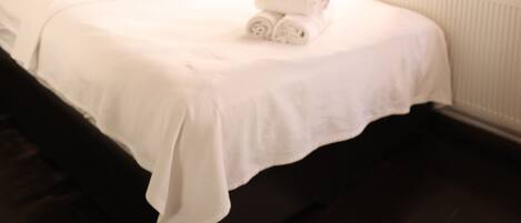 A bedroom with a wooden headboard, a bed with white linens, an orange curtain, and a white radiator.