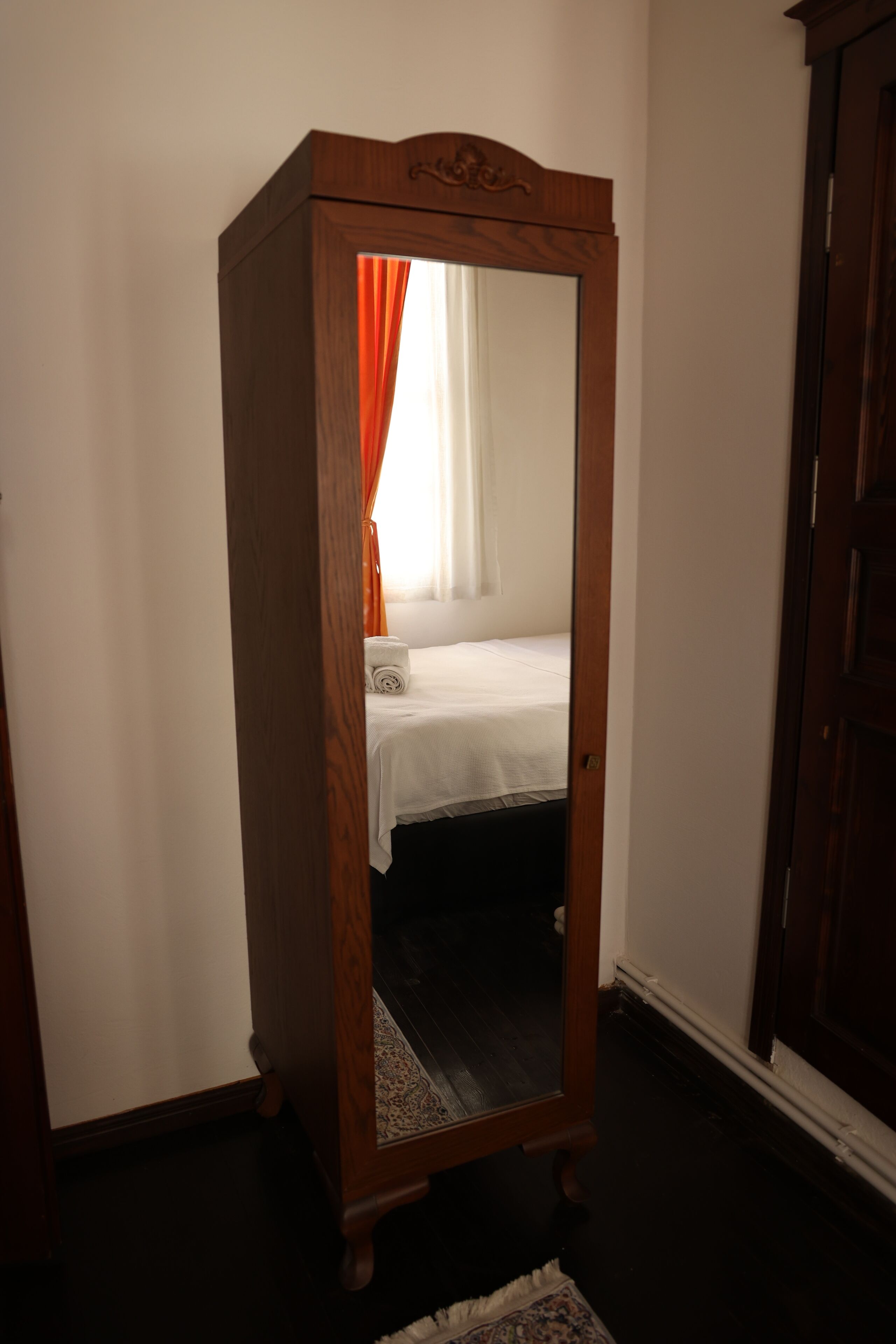 A wooden wardrobe with a mirror, a bed with white bedding, and a patterned rug.
