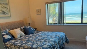 A bedroom with a bed, a window with a view, a ceiling fan, and a framed picture on the wall.