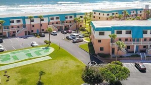 A beachfront hotel with multiple-story buildings, parking, and a view of the ocean.