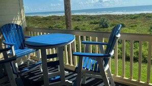 A covered outdoor area with a table and chairs, overlooking a beach.