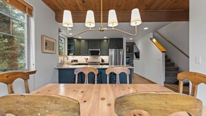 Eine moderne Küche mit Holzbalkendecke, einer zentralen Kochinsel mit Barhocker und einem Essbereich mit Holztisch und Stühlen.