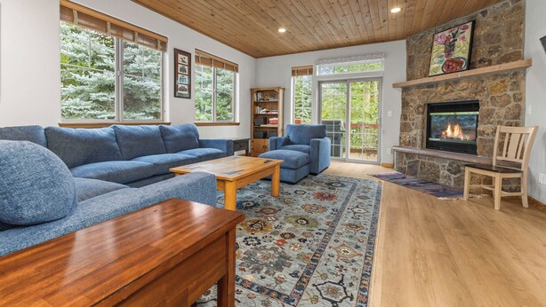 Ein gemütliches Wohnzimmer mit Kamin aus Stein, großen Fenstern und einem blauen Sofa.