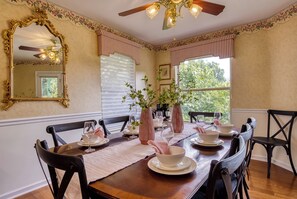 Comedor con mesa de madera dispuesta para cuatro personas, sillas a ambos lados, un espejo grande y un ventilador de techo.