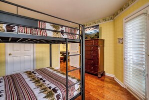 Una litera con ropa de cama estampada, un aparador, una puerta y una ventana con persianas.