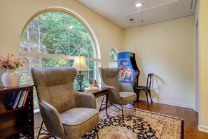 Una habitación con dos sillones de cuero, una estantería, una lámpara y un ventanal con vistas a árboles.