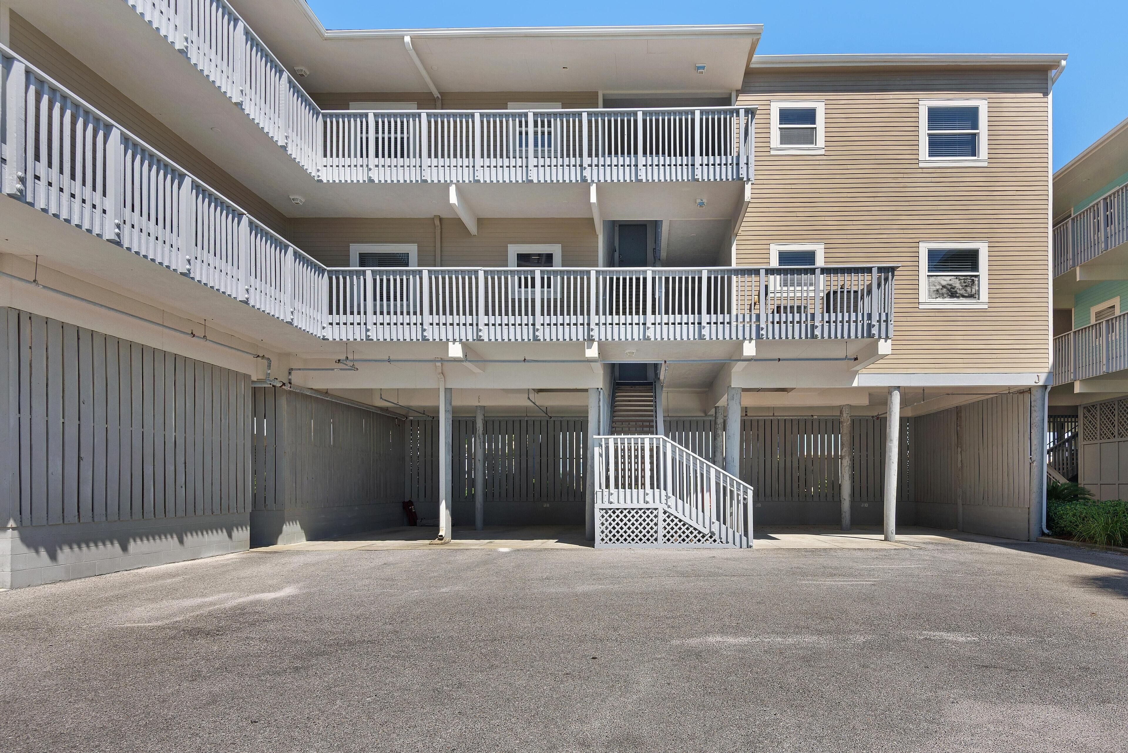 A multi-story residential building with balconies, a covered parking area, and a gated entrance.
