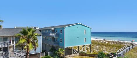 A beachfront property with a two-story building, a staircase leading to a balcony, and a view of the ocean.