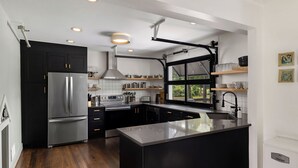 A modern kitchen with black cabinetry, stainless steel appliances, and a large island. - Modal House: A Fun-Filled Designer Home Just Steps from Downtown Main Street (Greenville)