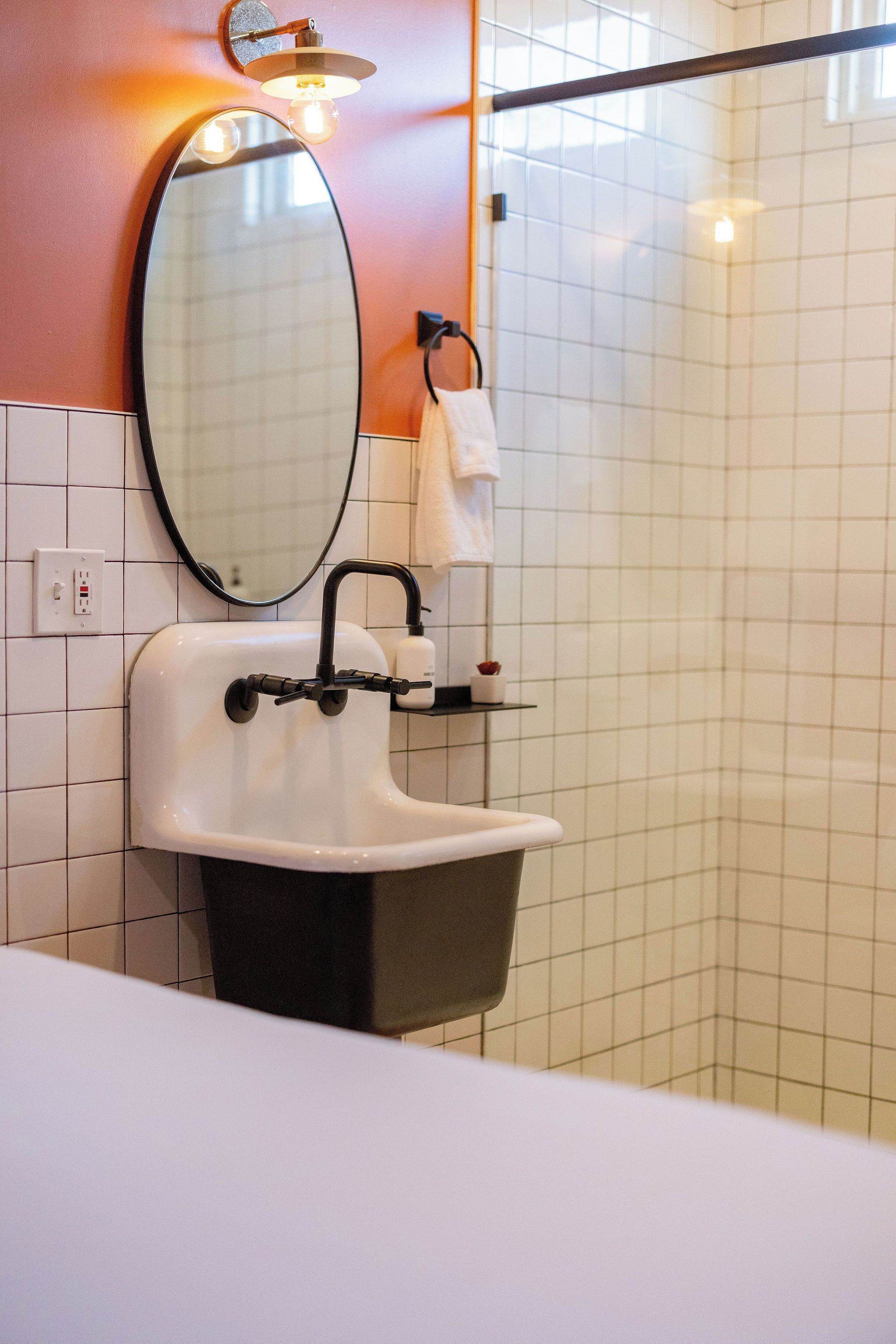 A bathroom with a white sink, black faucet, and a mirror with a light fixture above it.