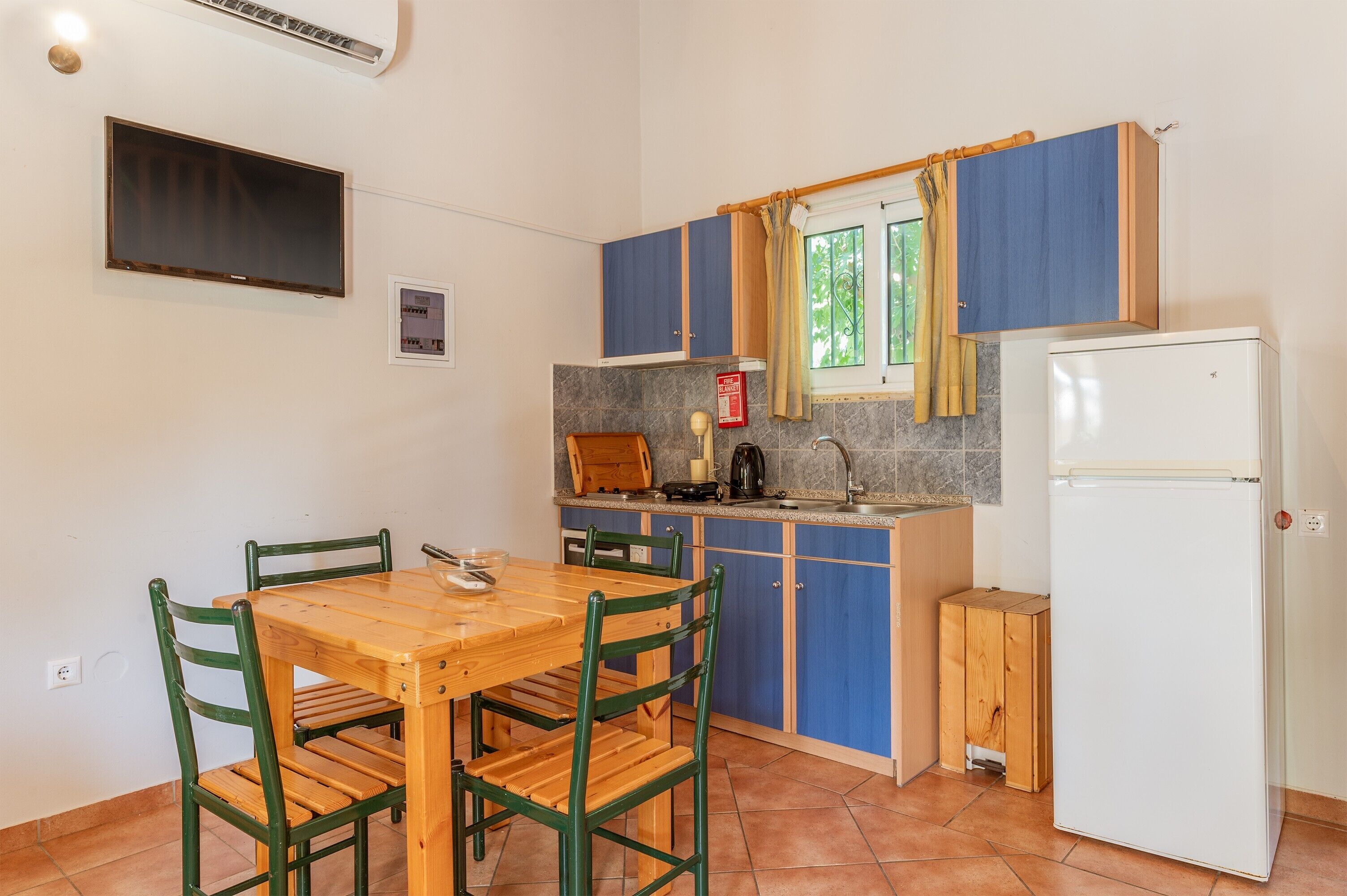 A compact kitchen with a wooden table and chairs, a built-in oven, and a white refrigerator.