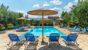 Una piscina con sillas de descanso azules y sombrillas de paja.