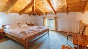 Un dormitorio con techo de madera, una cama, una mesita de noche, una ventana con cortinas y un banco de madera.
