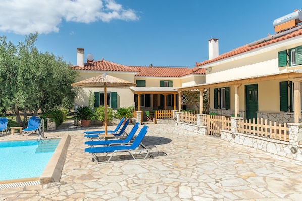 A pool area with lounge chairs, a stone patio, and a building with a tiled roof.