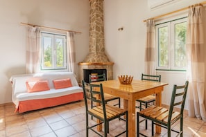 Una habitación acogedora con chimenea de piedra, una mesa de madera con sillas, un sofá con cojines y ventanas con cortinas.