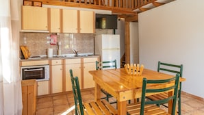 Una cocina con armarios de madera, una mesa de comedor con sillas, horno empotrado y un televisor.