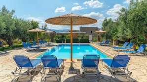 Una piscina con sillas de descanso azules y sombrillas de paja.
