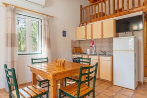 Une cuisine avec une table et des chaises en bois, un réfrigérateur et une fenêtre avec des rideaux.