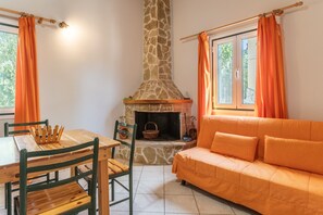 A cozy room with a stone fireplace, a wooden table with chairs, and an orange sofa.
