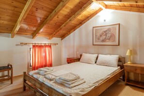 A bedroom with a wooden ceiling, a bed with folded towels, a nightstand, a lamp, and a painting on the wall.