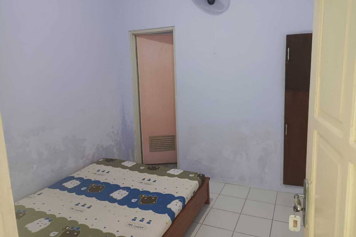 A small bedroom with a single bed, a door, and a wall-mounted fan.
