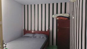Habitación individual con una pared a rayas, un ventilador de techo, un equipo de aire acondicionado y una alfombra verde.