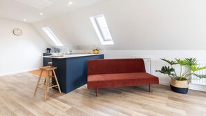 A modern kitchen with a red sofa, wooden stools, and a potted plant. - Beautiful Self Contained Annex in Toddington (Cheltenham)
