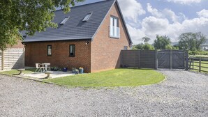 A single-story brick house with a sloped roof, a small patio with outdoor furniture, and a gravel driveway. - Beautiful Self Contained Annex in Toddington (Cheltenham)