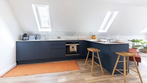 A modern kitchen with dark blue cabinetry, a marble countertop, and two wooden stools. - Beautiful Self Contained Annex in Toddington (Cheltenham)